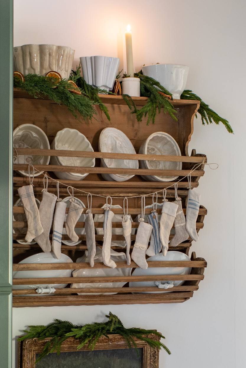 vintage-wooden-rack-with-mini-christmas-stockings-white-ceramics-greenery-and-candlelit-holiday-decor