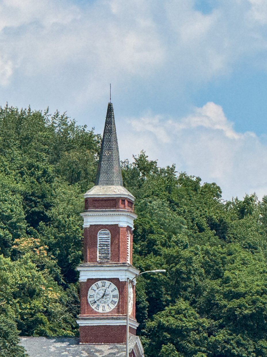 historic-brick-clock-tower-with-peaked-roof-surrounded-by-lush-green-trees-and-foliage-royalty-free-photo