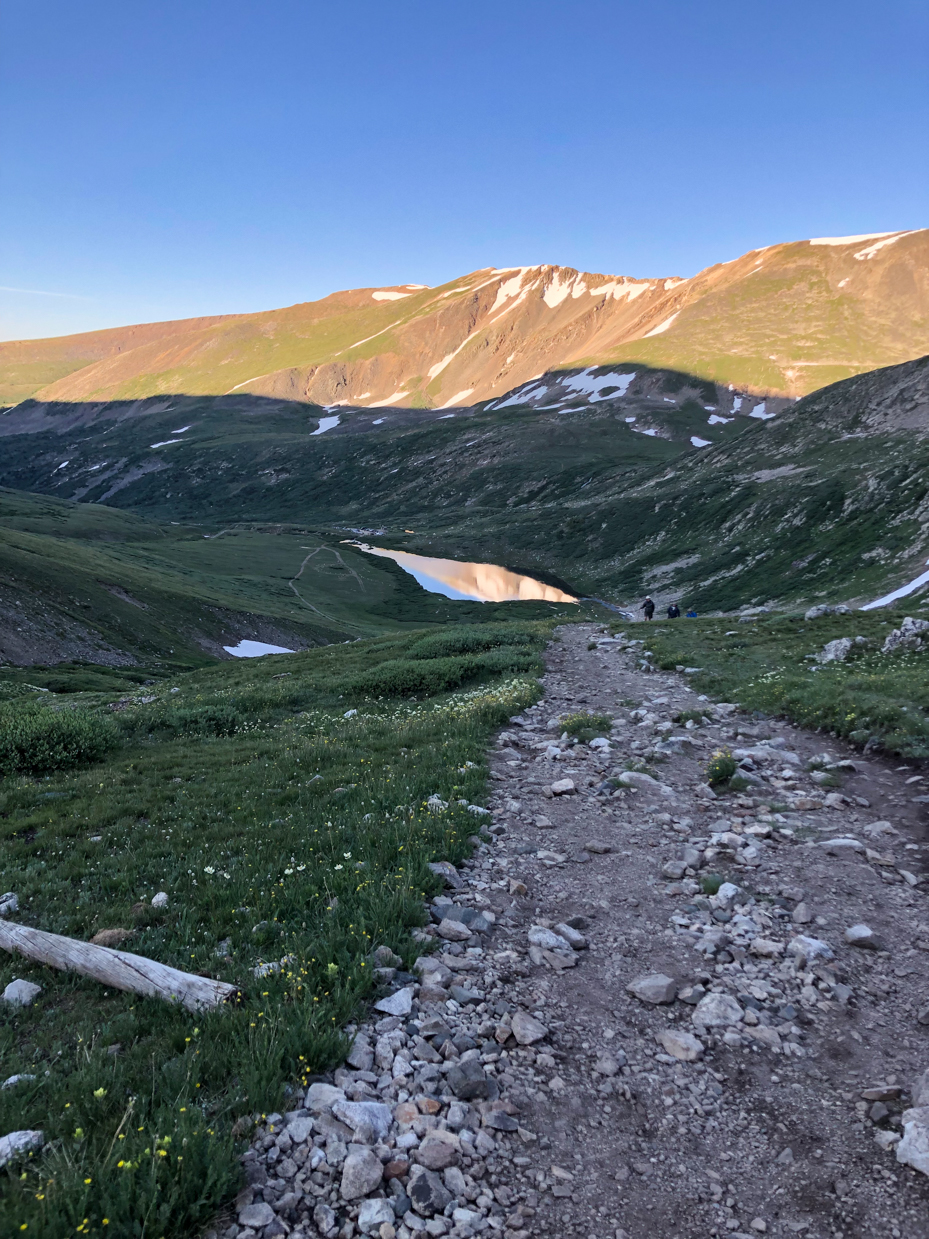 mountain-trail-at-sunset-with-snow-capped-peaks-and-alpine-lake-reflection