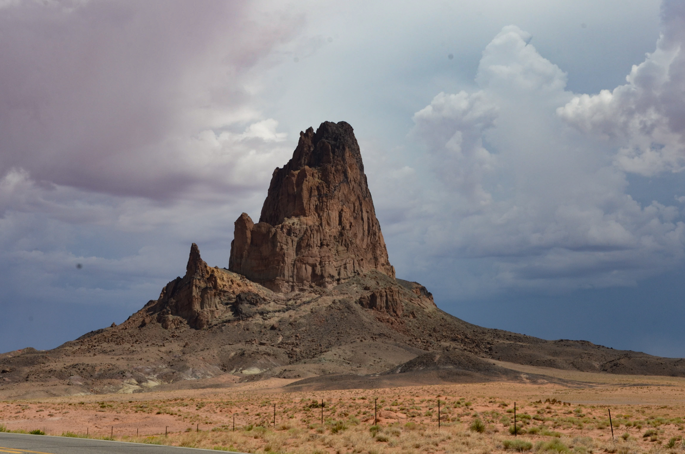 towering-agathla-peak-dominating-arid-desert-landscape-under-dramatic-clouds