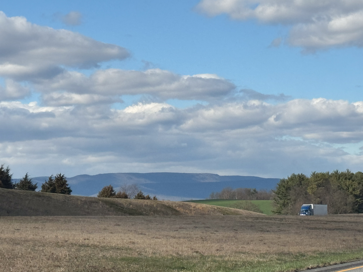 rolling-farmland-with-truck-distant-blue-mountains-and-dramatic-cloudy-sky-countryside-scenic-overlook-royalty-free-photo