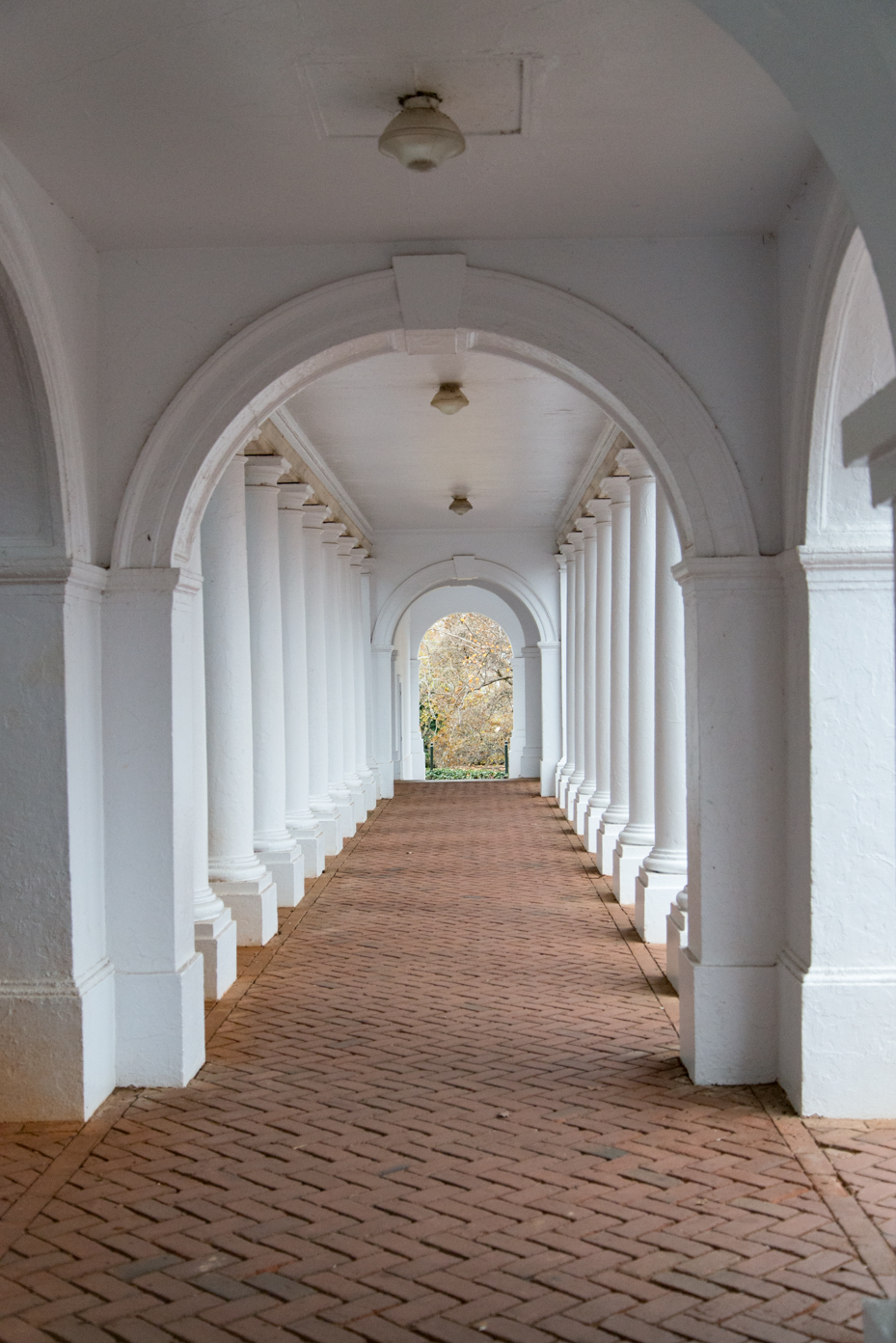 arched-classical-corridor-with-white-columns-and-herringbone-brick-path