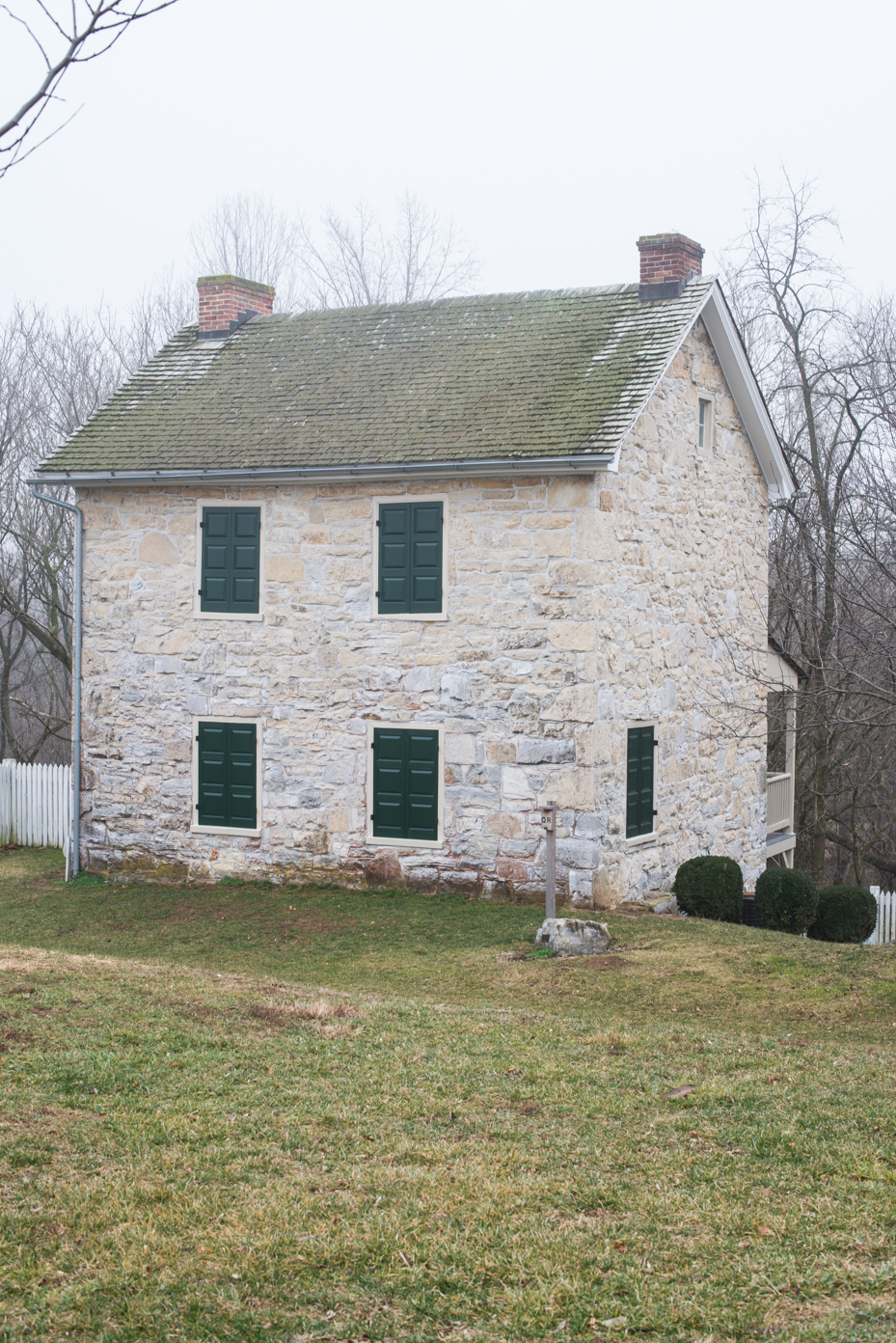 colonial-stone-house-with-green-shutters-historic-architecture-with-brick-chimneys-and-moss-covered-roof