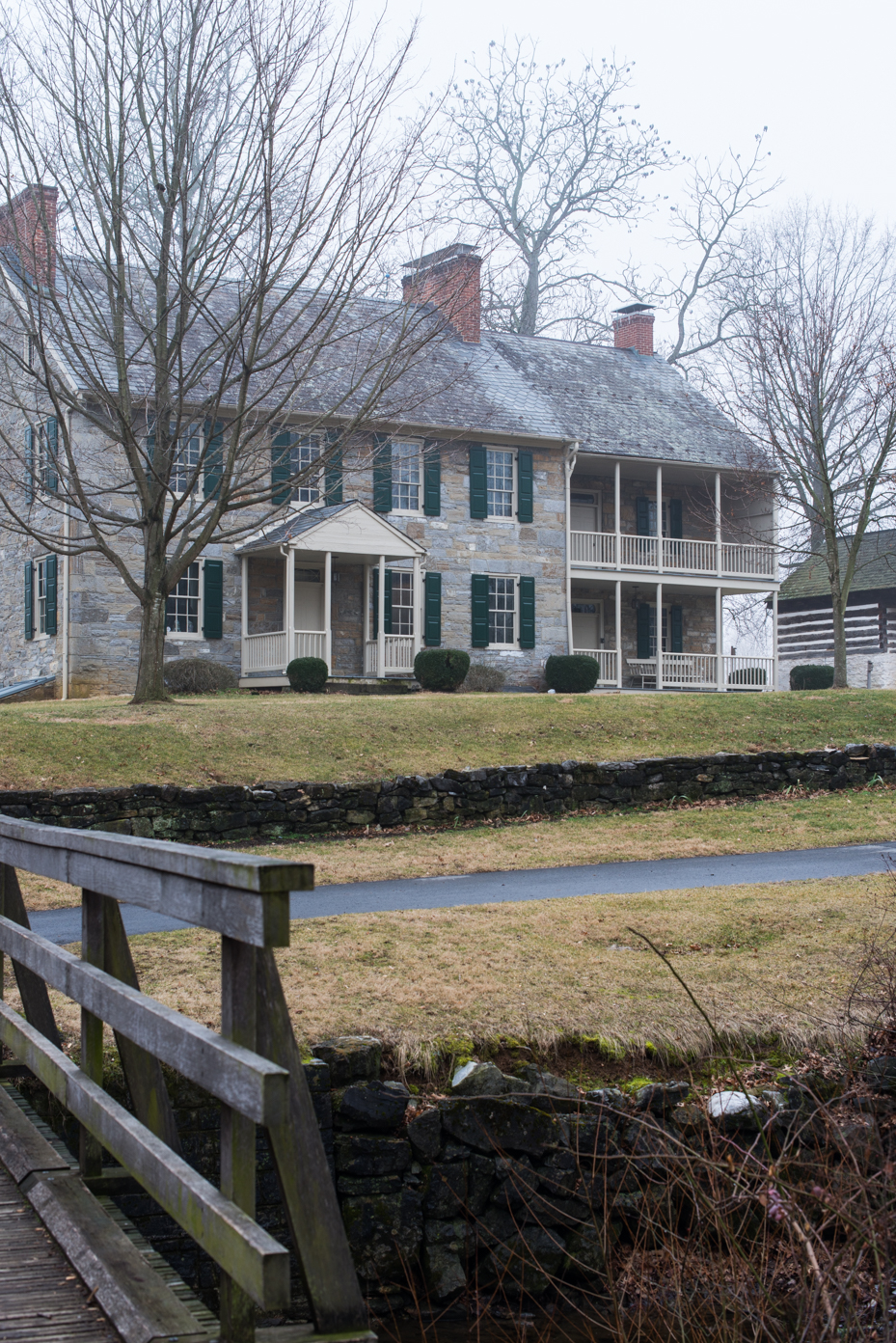 historic-colonial-manor-with-terraced-grounds-stone-house-featuring-double-porches-green-shutters-and-wooden-bridge-access