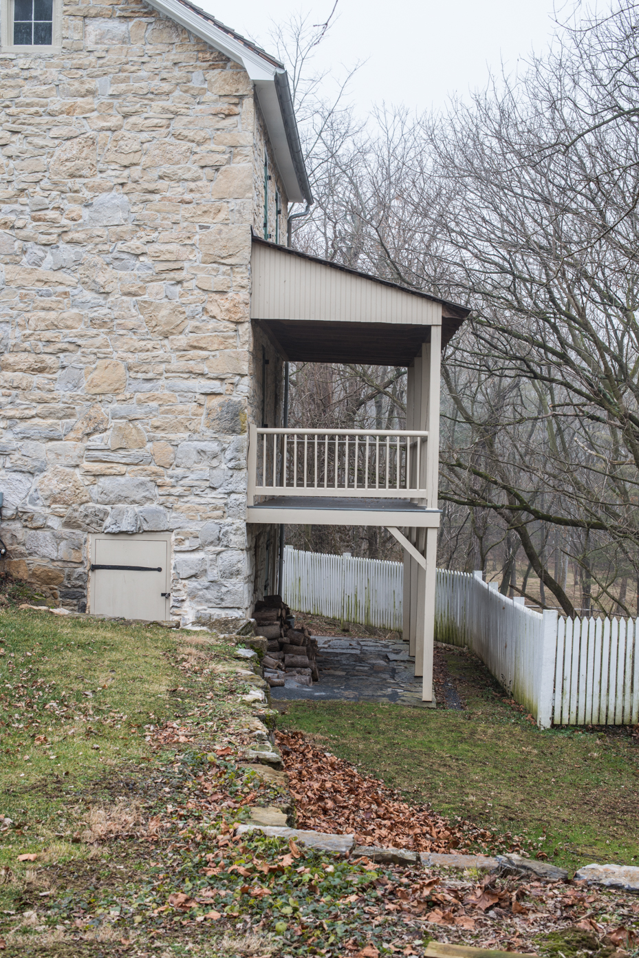 historic-stone-house-with-covered-porch-limestone-exterior-with-white-picket-fence-and-fall-leaves