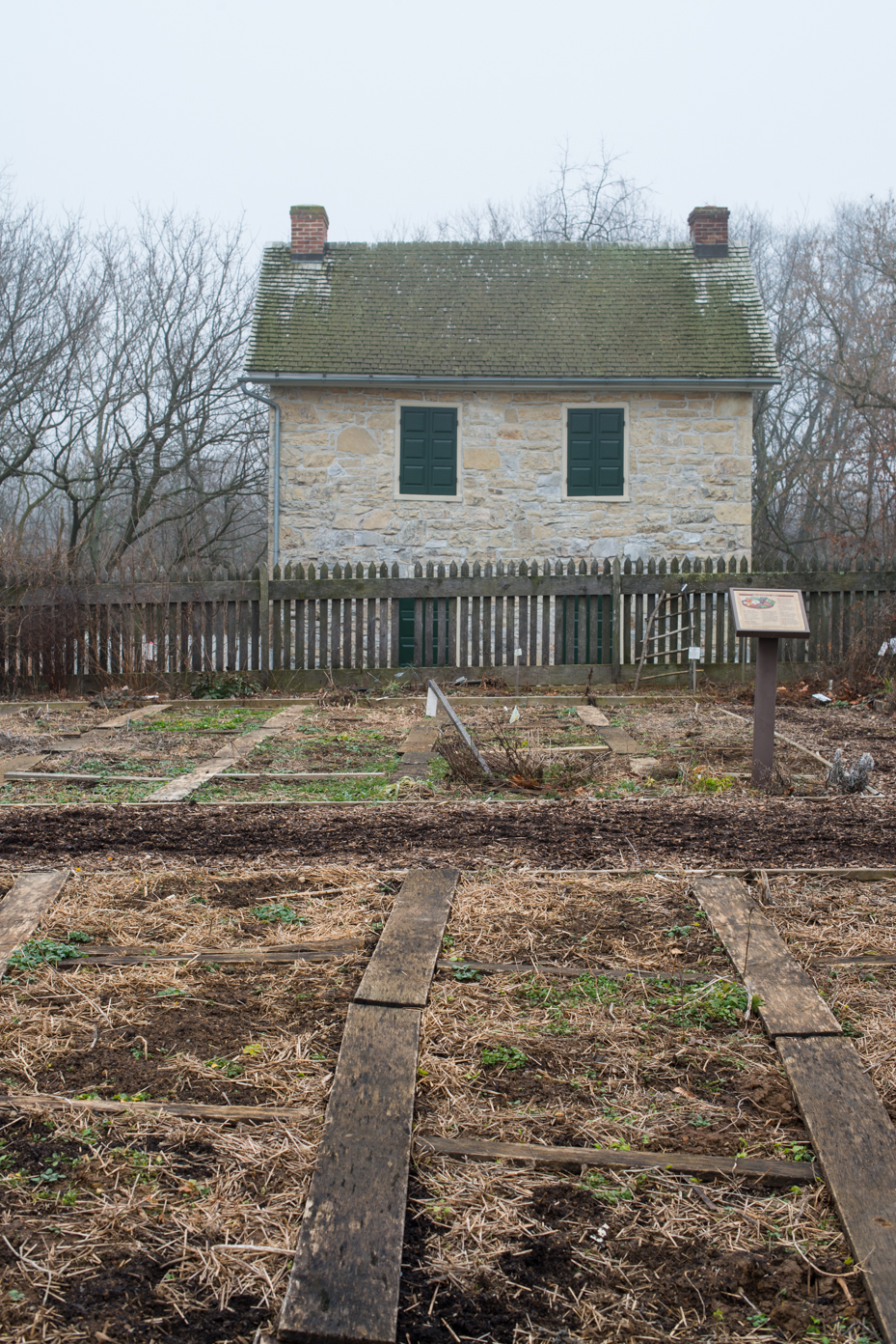 historic-stone-house-with-heritage-garden-plot-colonial-architecture-with-wooden-garden-beds-and-picket-fence