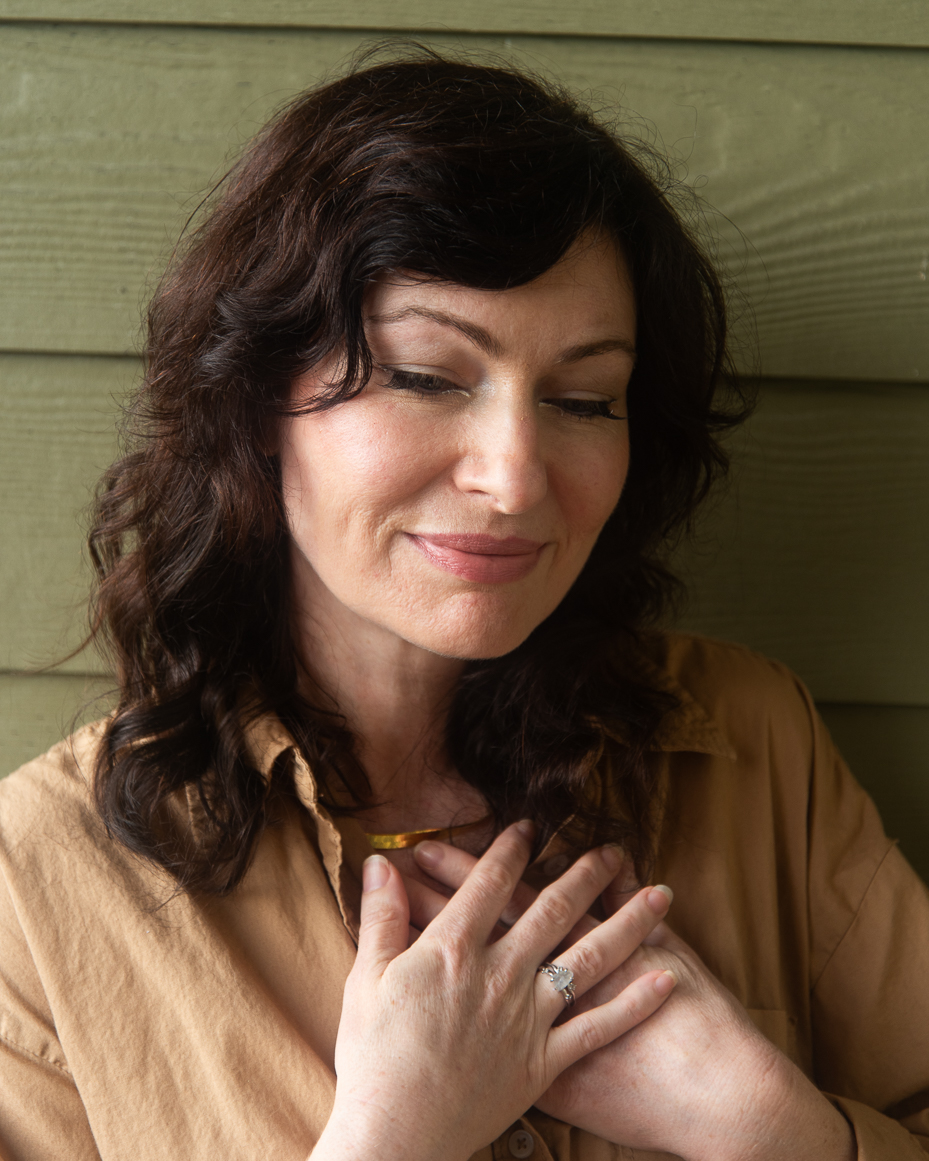 woman-with-dark-wavy-hair-in-tan-shirt-smiling-softly-with-hands-over-heart