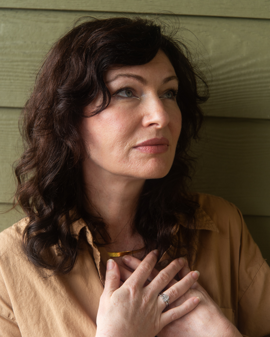woman-with-wavy-dark-hair-in-tan-shirt-gazing-upward-with-hands-on-chest