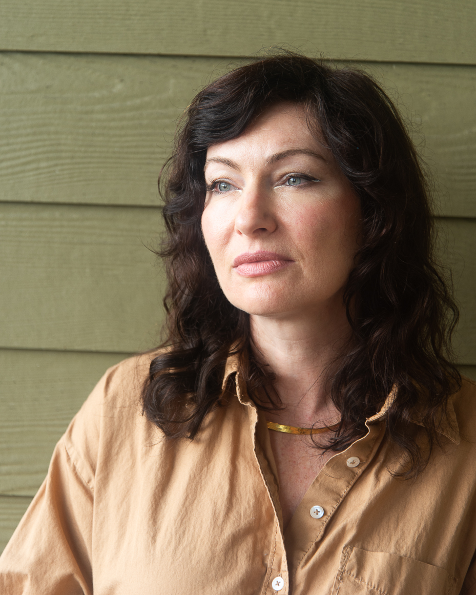 woman-with-wavy-dark-hair-in-tan-shirt-looking-thoughtfully-into-distance