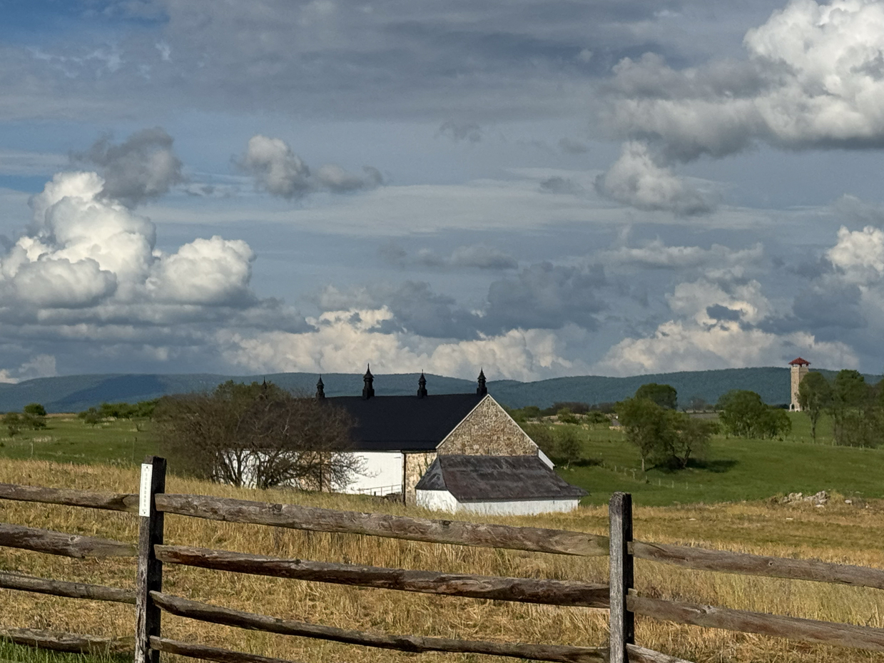 black-roofed-stone-barn-with-split-rail-fence-under-a-dramatic-cloudy-sky-artist-reference-photo