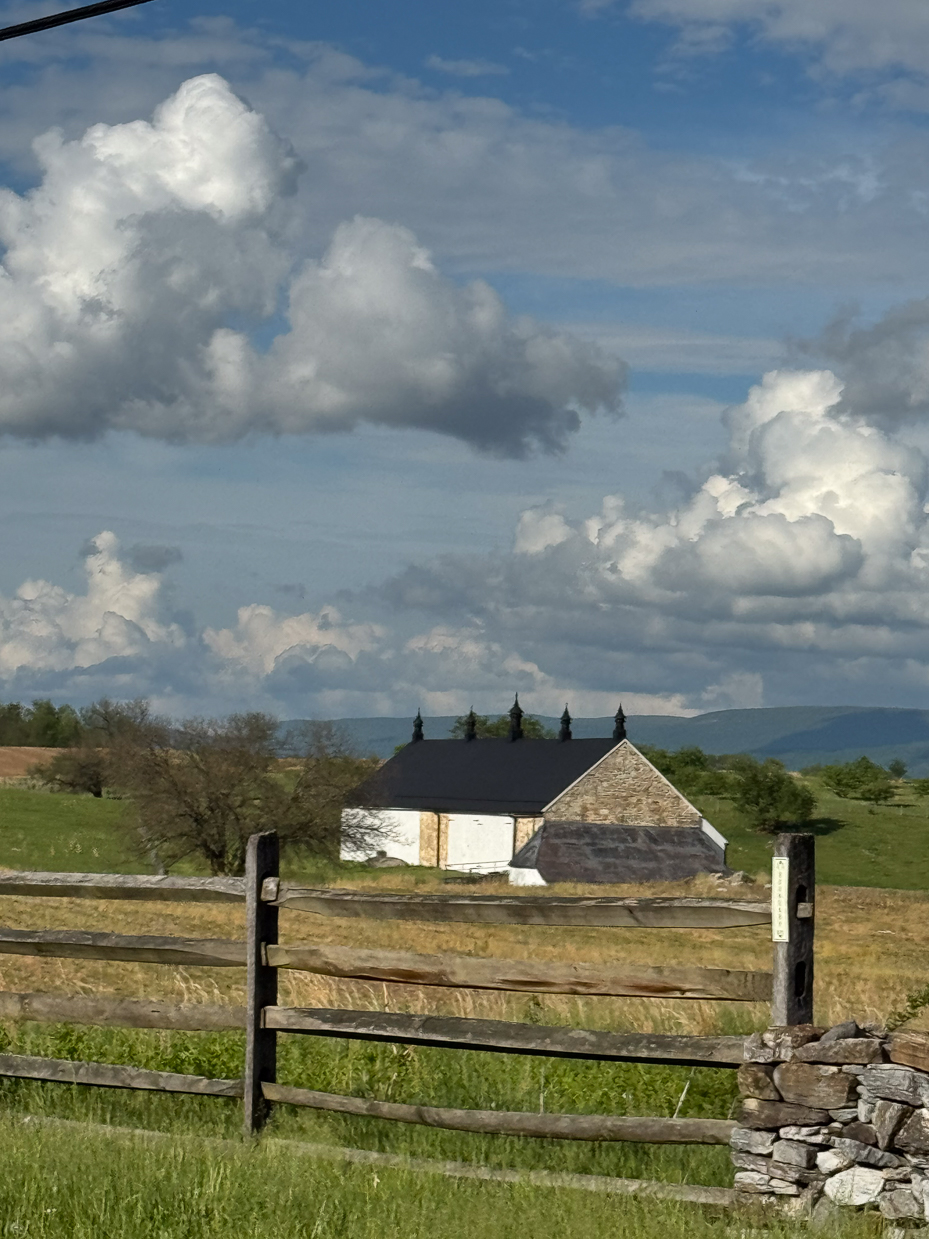 white-barn-with-black-roof-and-cloud-filled-sky-behind-wooden-fence-artist-reference-photo
