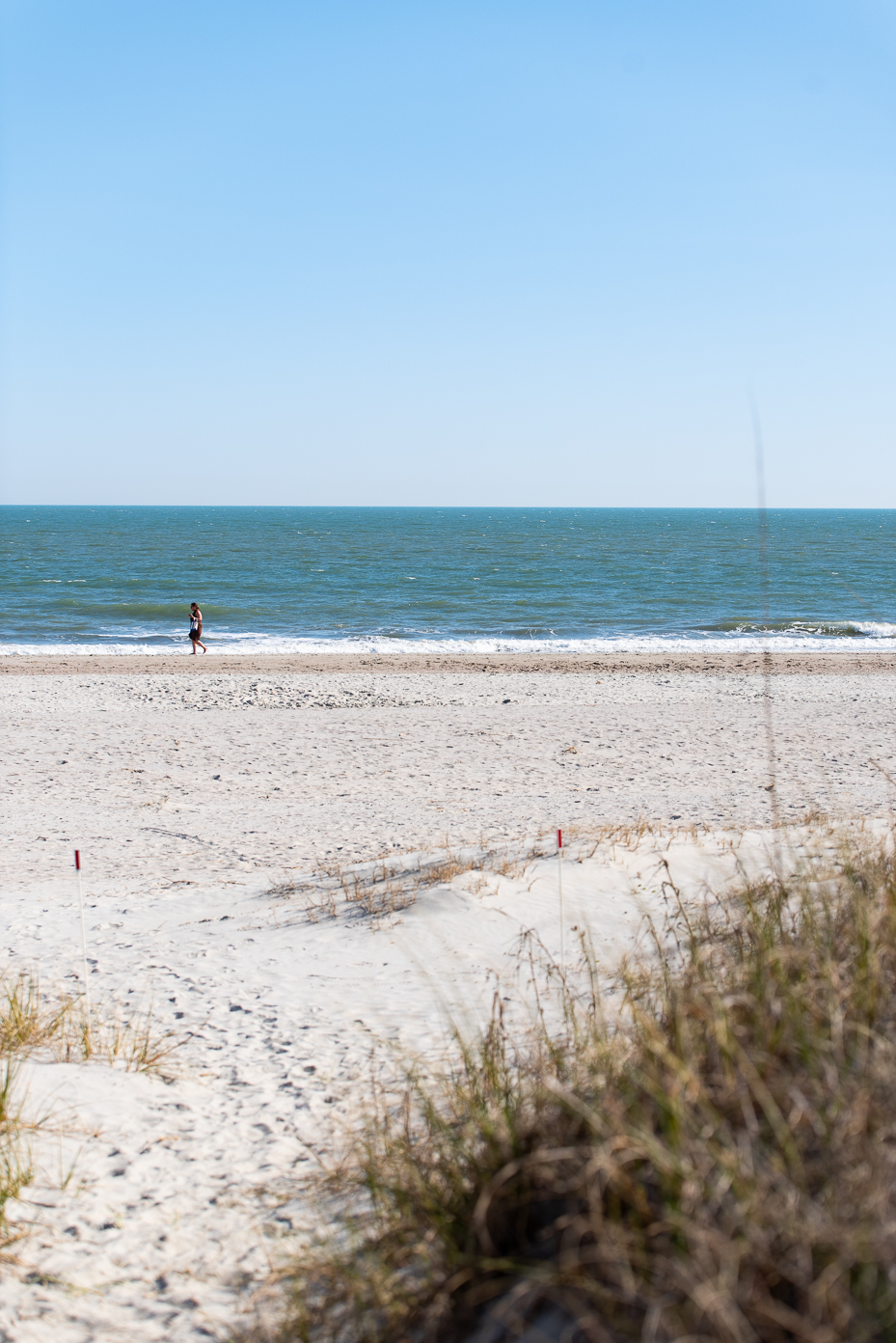 peaceful-beach-scene-with-lone-person-walking-by-ocean-under-clear-blue-sky