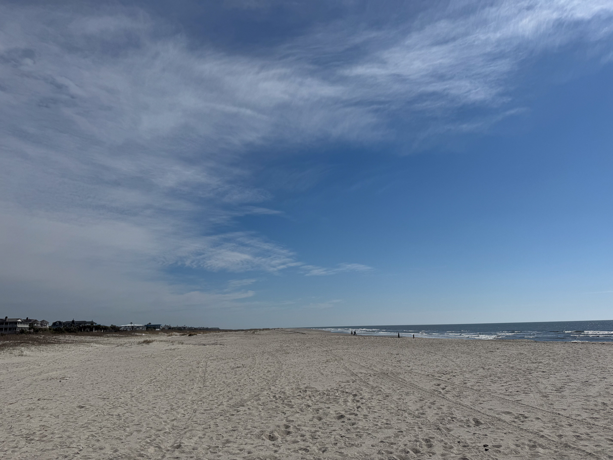 peaceful-sandy-beach-with-ocean-waves-and-scattered-beachgoers-under-a-blue-sky-with-wispy-clouds