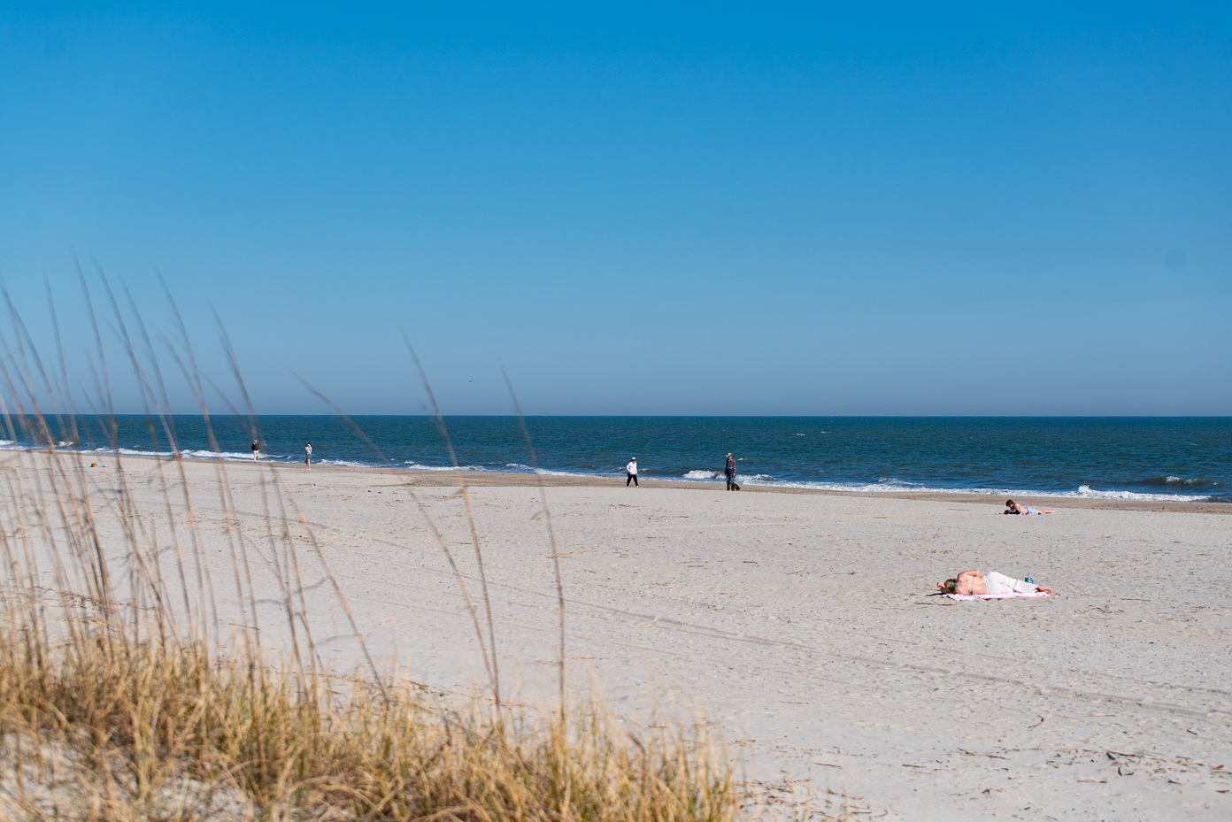 people-relaxing-and-walking-on-a-peaceful-beach-with-clear-blue-sky-and-ocean-horizon