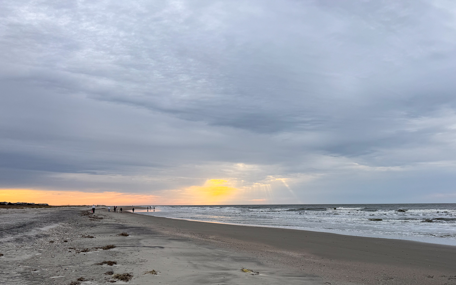 stormy-beach-sunset-with-golden-sun-rays-and-distant-shoreline-walkers