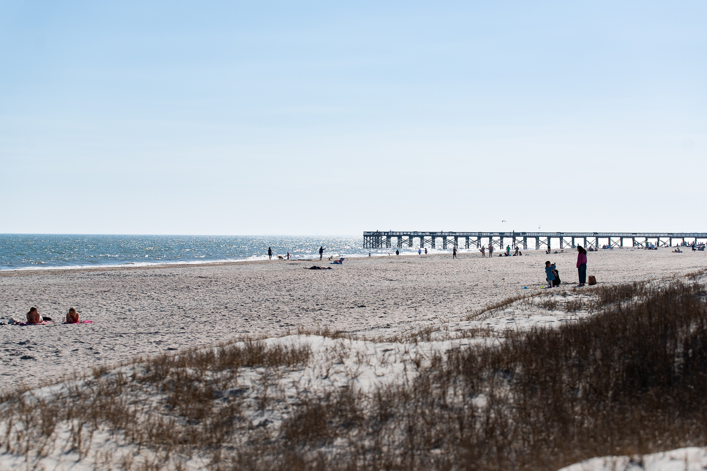 sunny-beach-scene-with-families-sunbathers-and-a-long-pier-extending-over-the-ocean