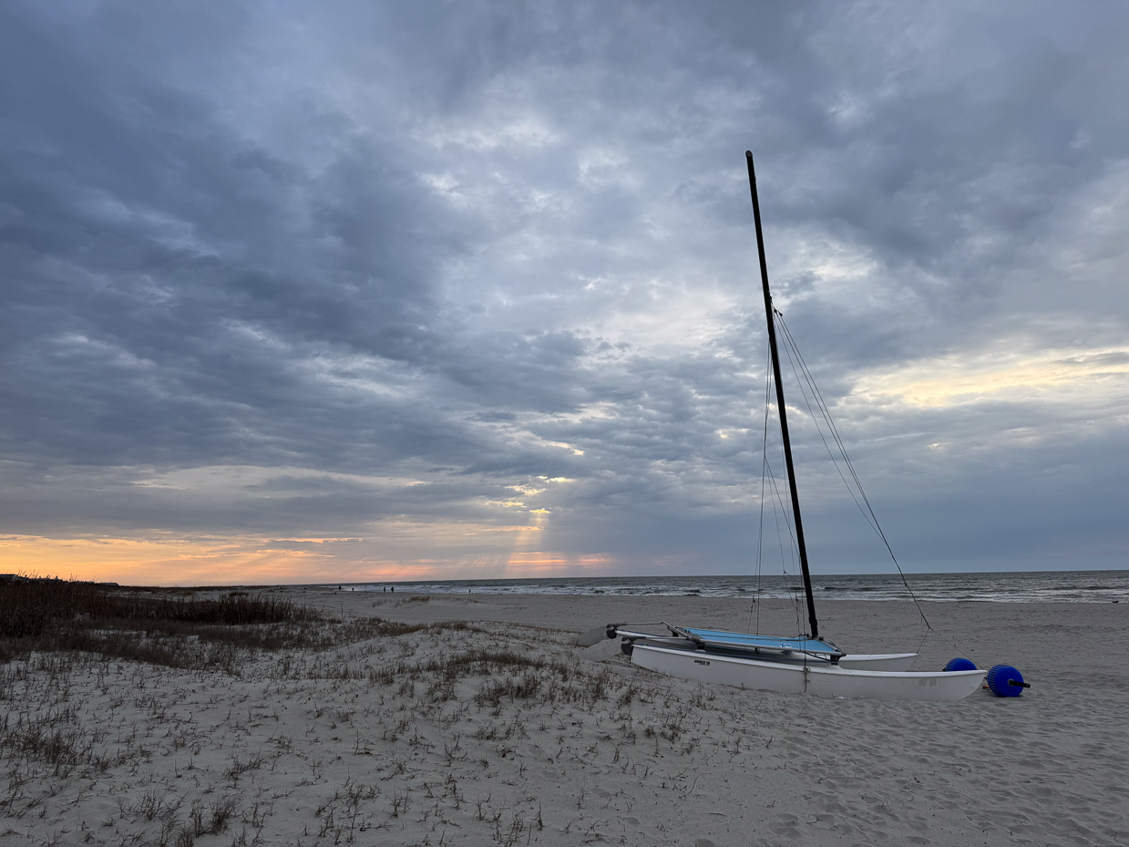 sunset-sailboat-on-beach-with-stormy-clouds-and-golden-light-breaking-through-over-ocean