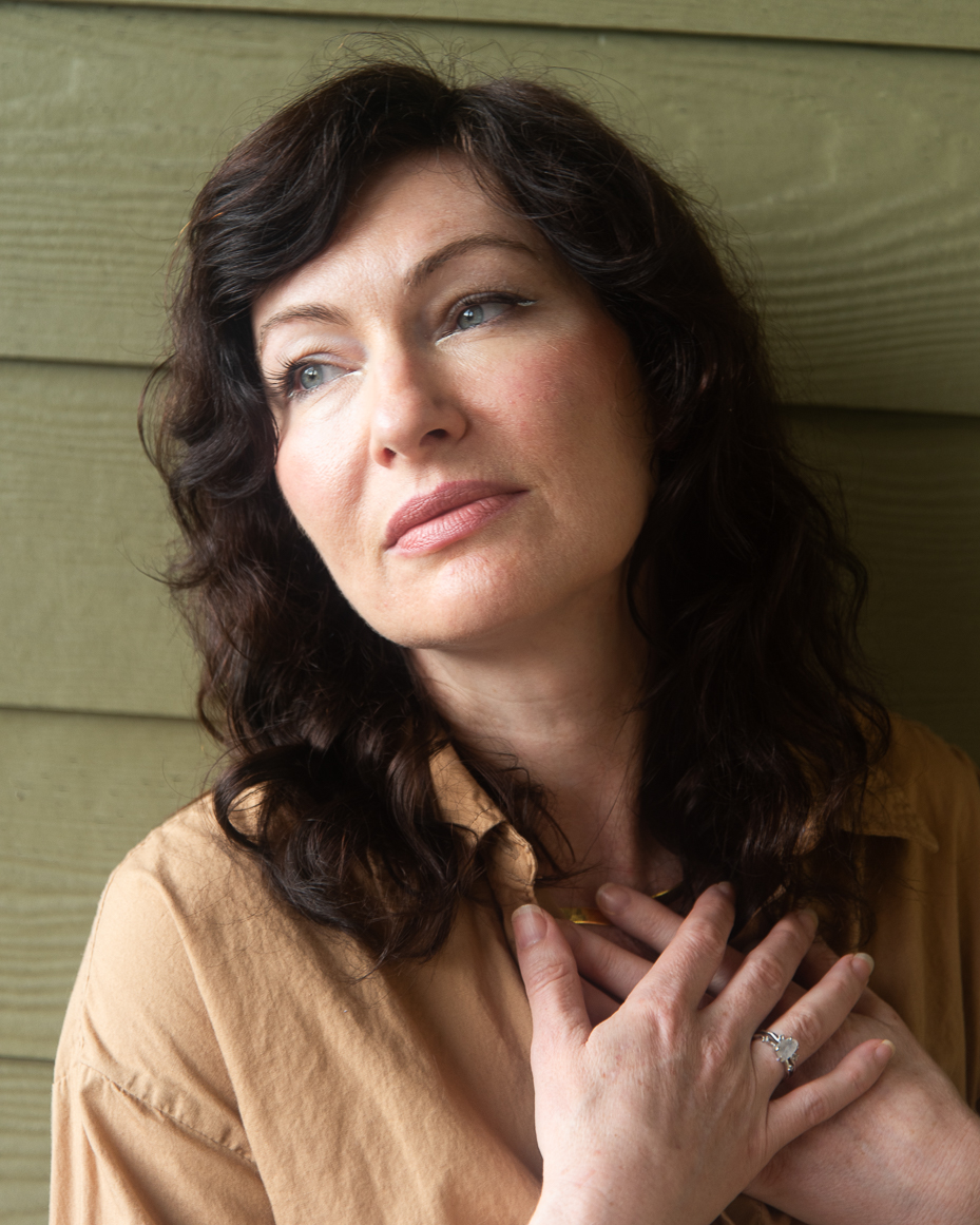 woman-with-dark-hair-in-tan-shirt-holding-chest-with-both-hands-and-looking-up