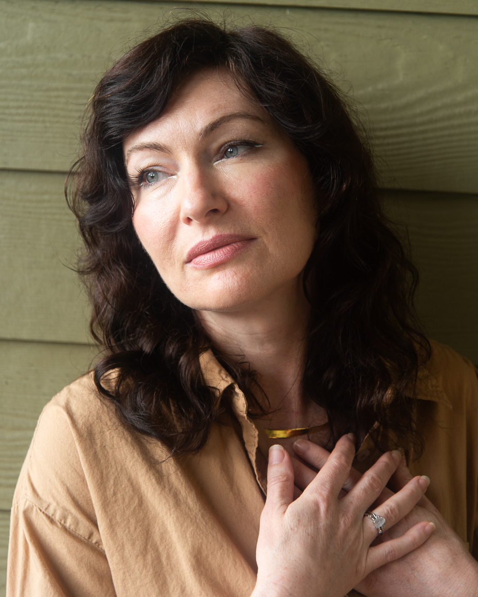 woman-with-dark-hair-in-tan-shirt-holding-chest-with-hands-and-looking-away-thoughtfully